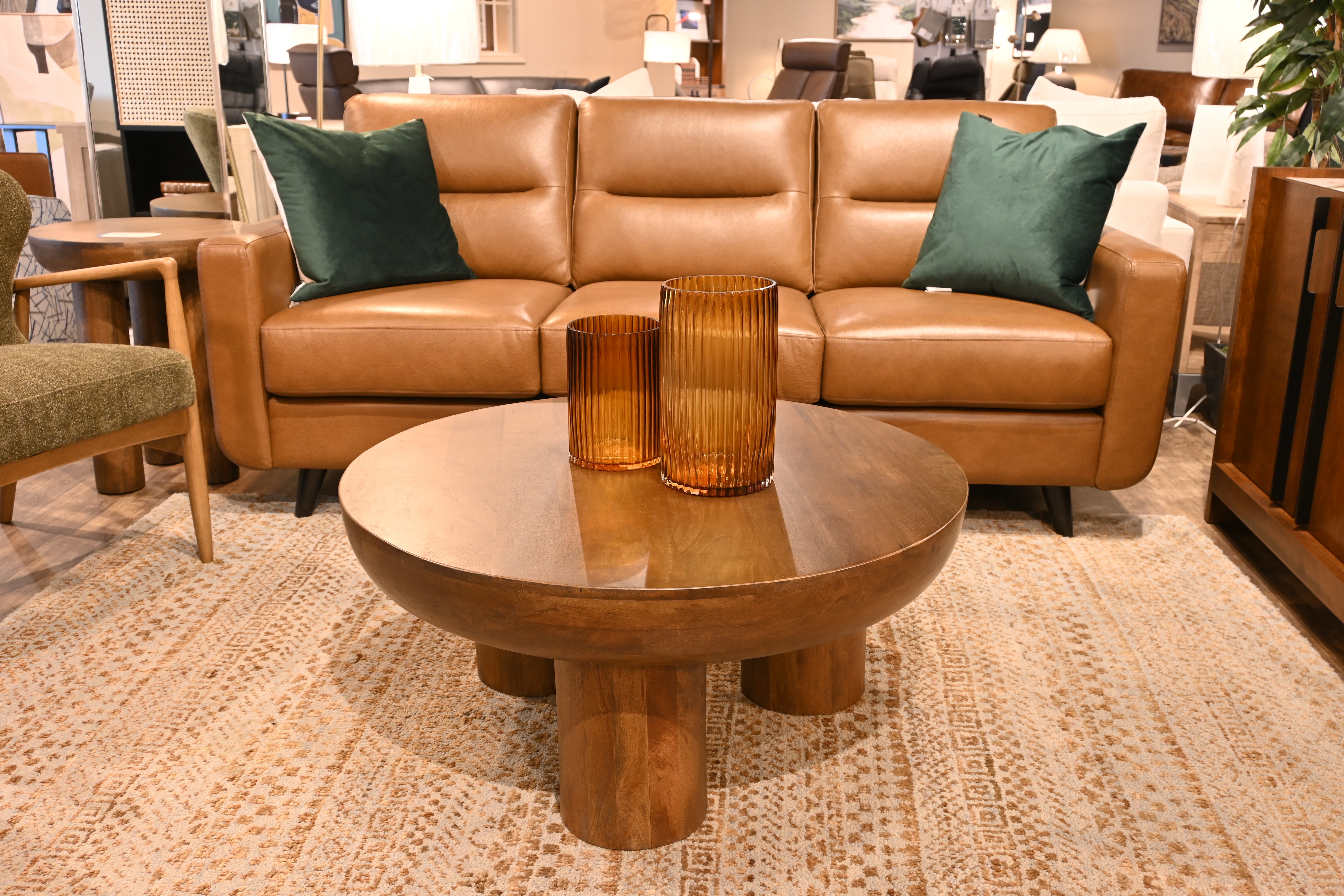 Brown leather sectional sofa with green pillows and a wooden coffee table in a room setting.