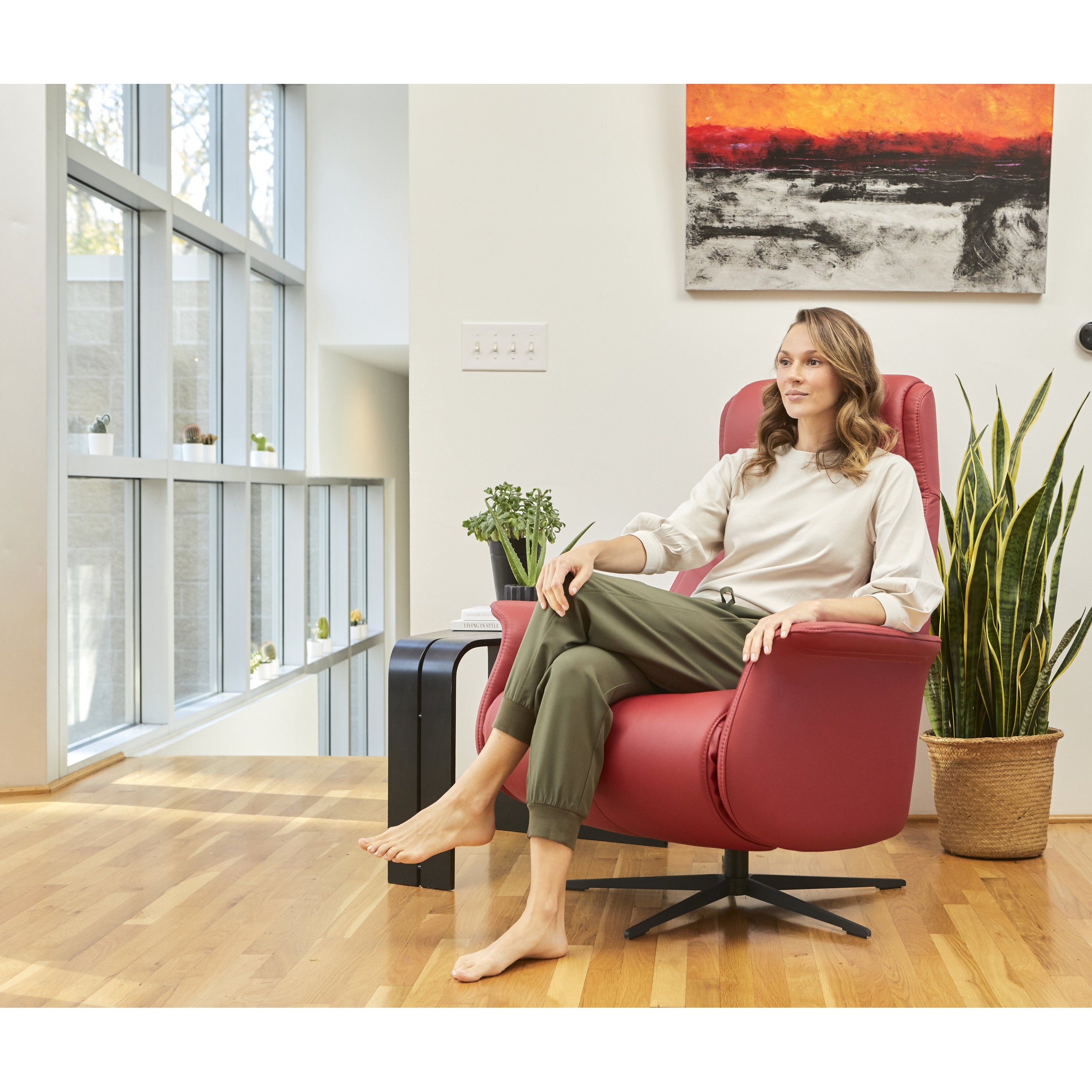 Woman sitting in a red armchair in a modern living room with large windows and plants.