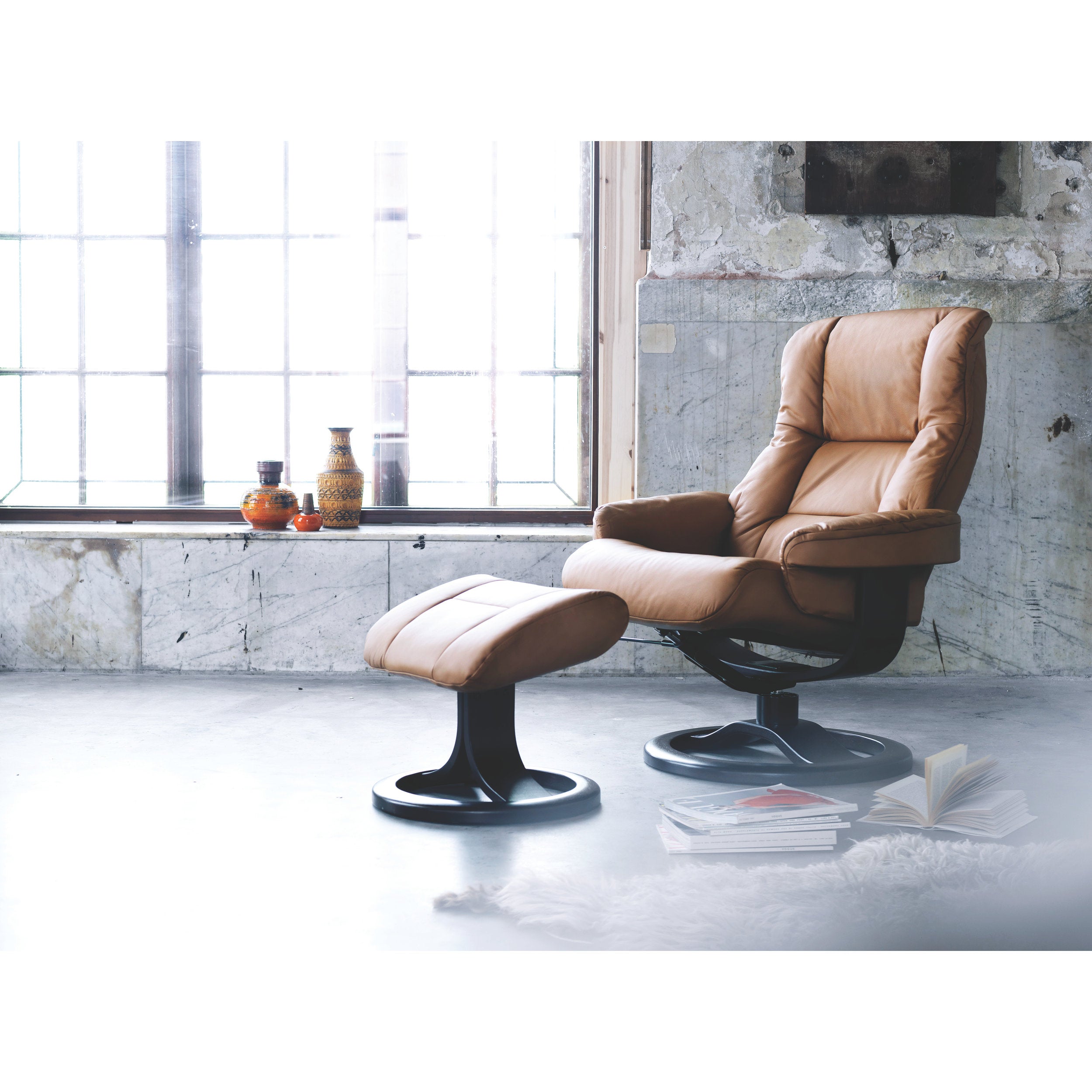 Brown leather recliner chair with ottoman in a room with large windows and exposed brick wall.