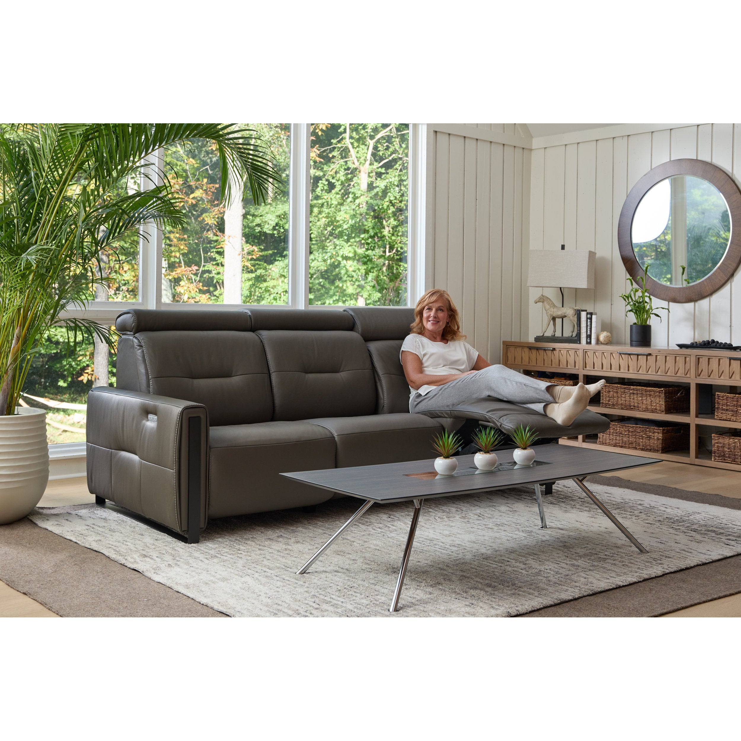 Woman sitting on a gray sectional sofa in a modern living room with a coffee table and decorative items.