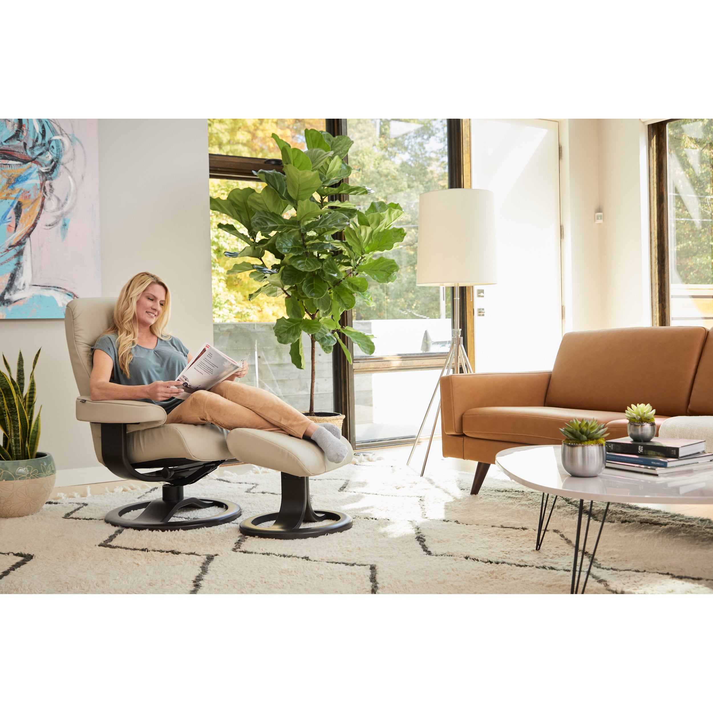 Woman reading a book in a modern living room with a brown sofa and decorative plants.
