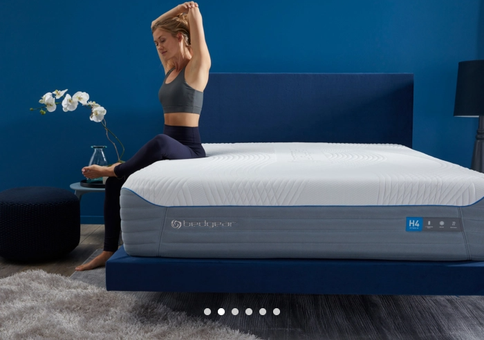 h4 mattress on a blue bedframe along a blue wall. Has a person sitting on it