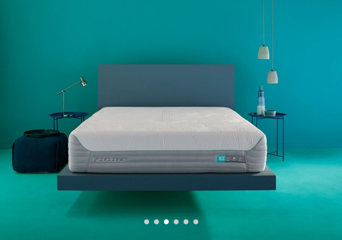 mattress on a floating blue bedframe. Mattress on top shows patterns and is along blue wall