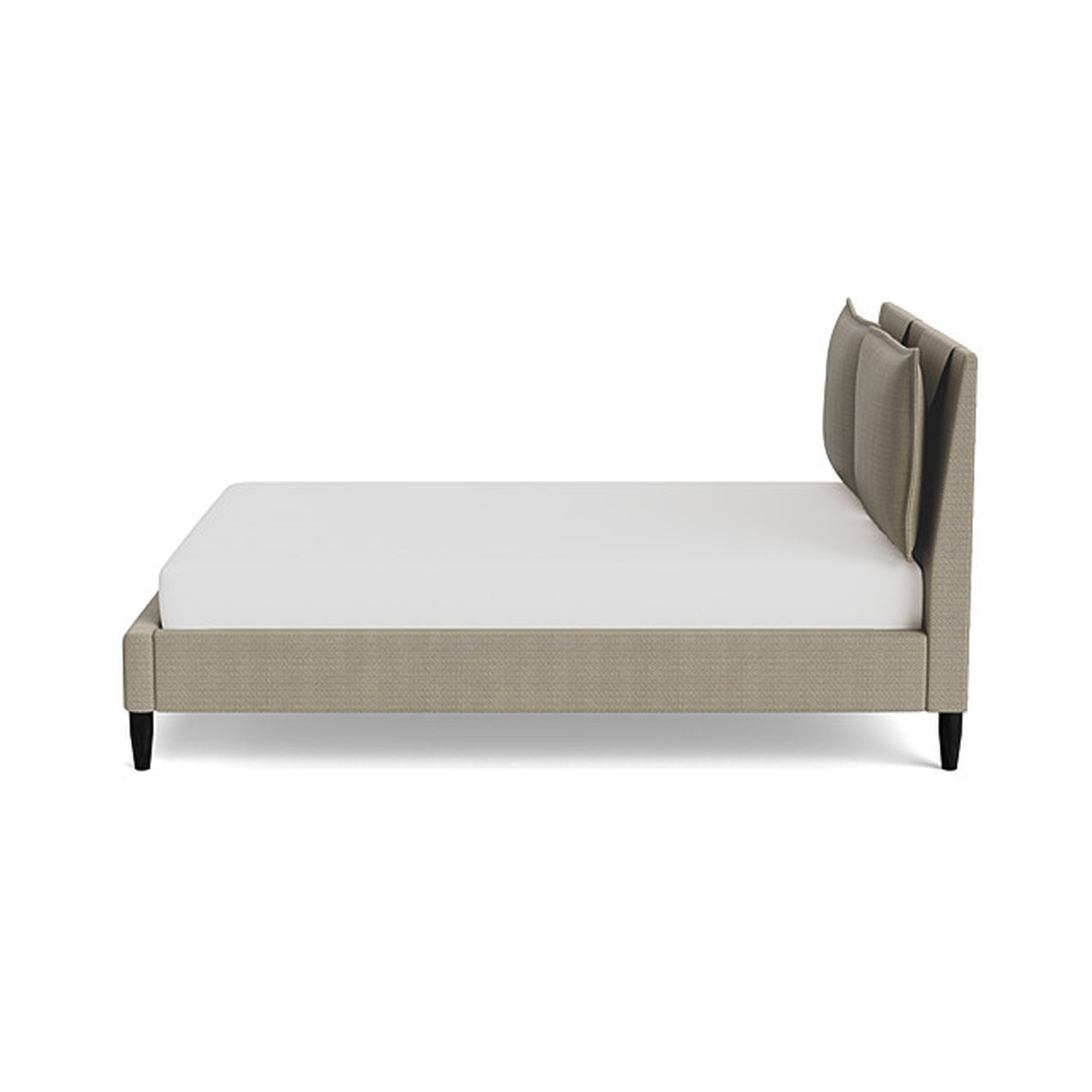 Stylus Sabine Bed in warm beige linen upholstery with padded multi-panel headboard, cream mattress, and black tapered legs.