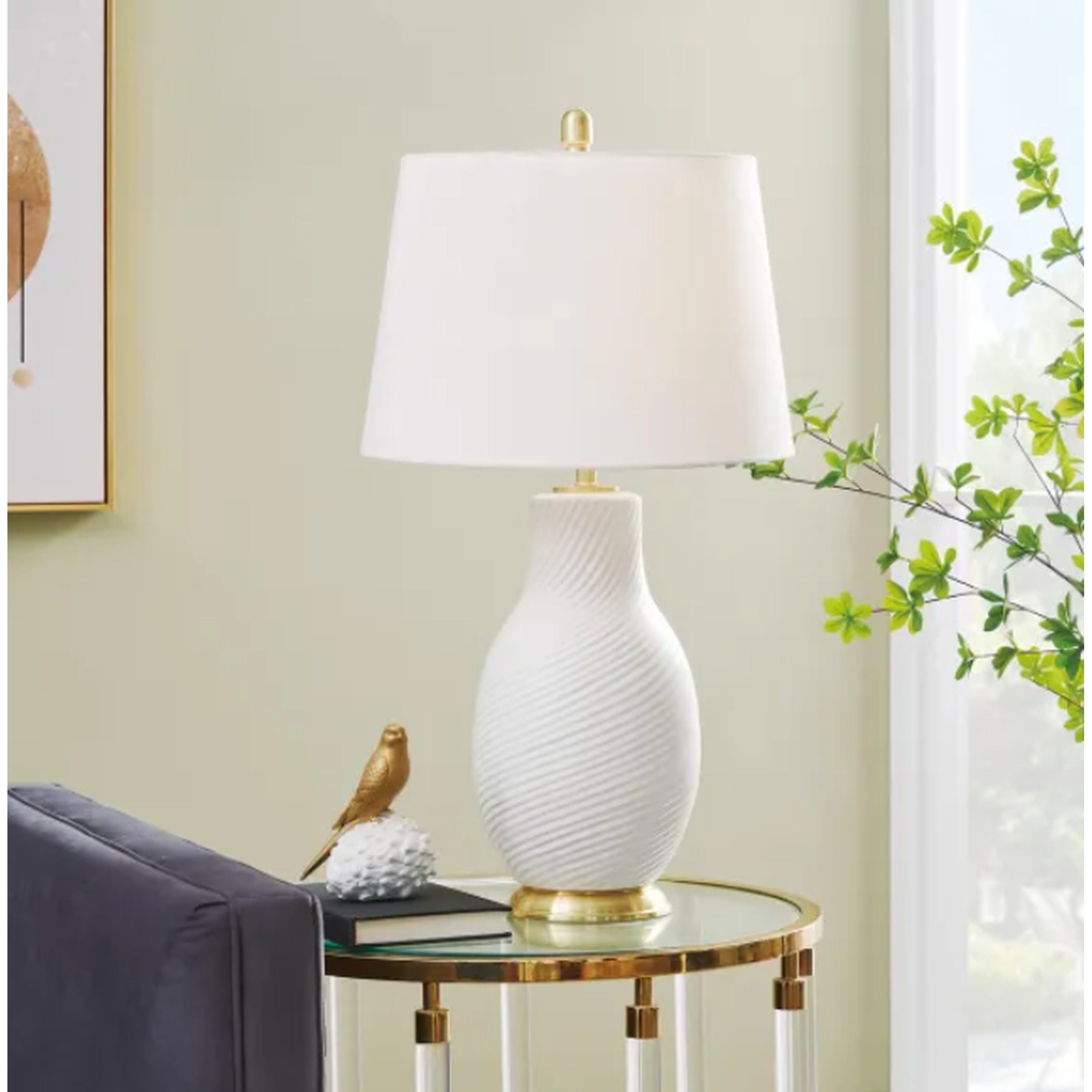 White textured table lamp on a glass side table with decorative items in a room setting.