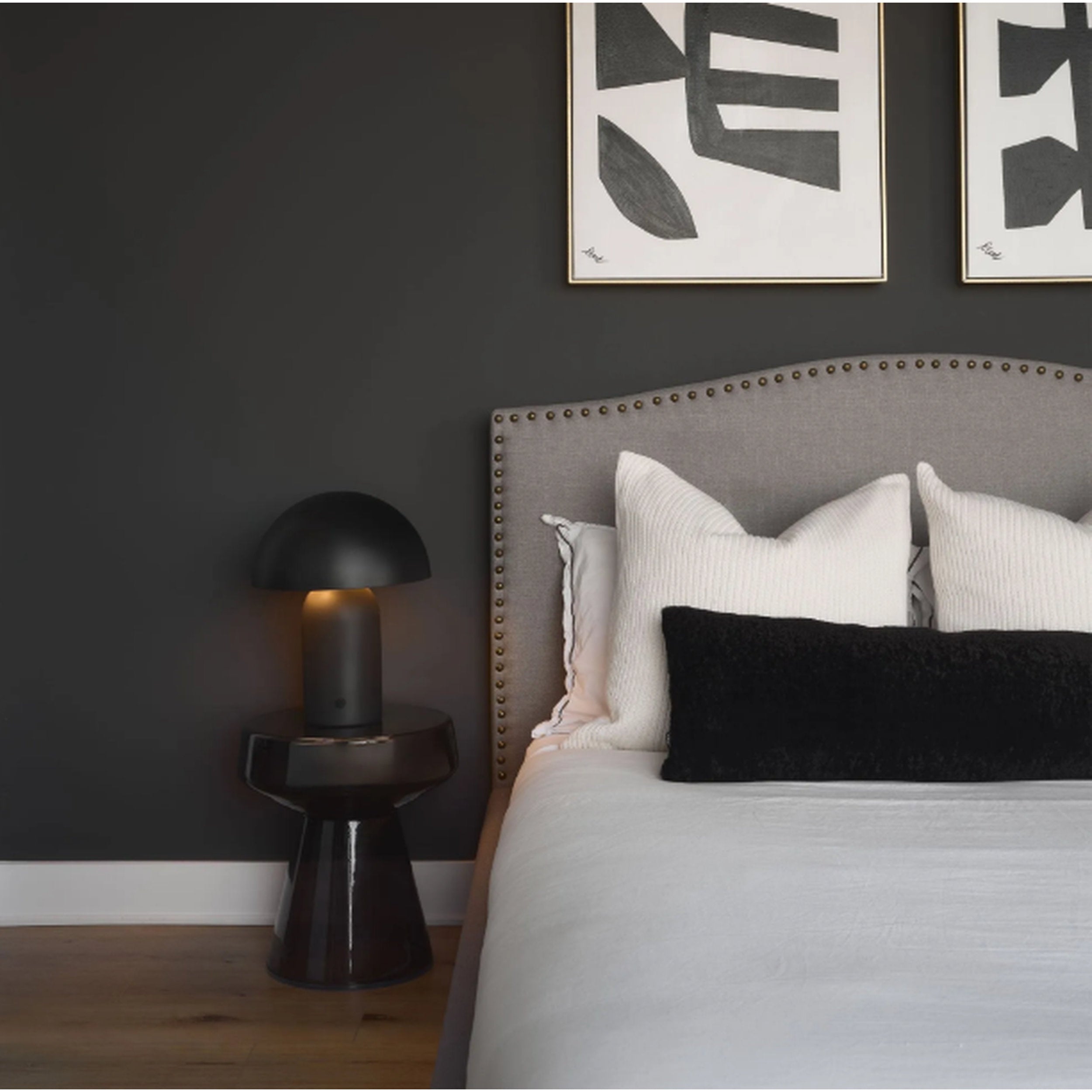 Modern bedroom with gray upholstered bed, black lamp, and abstract wall art.