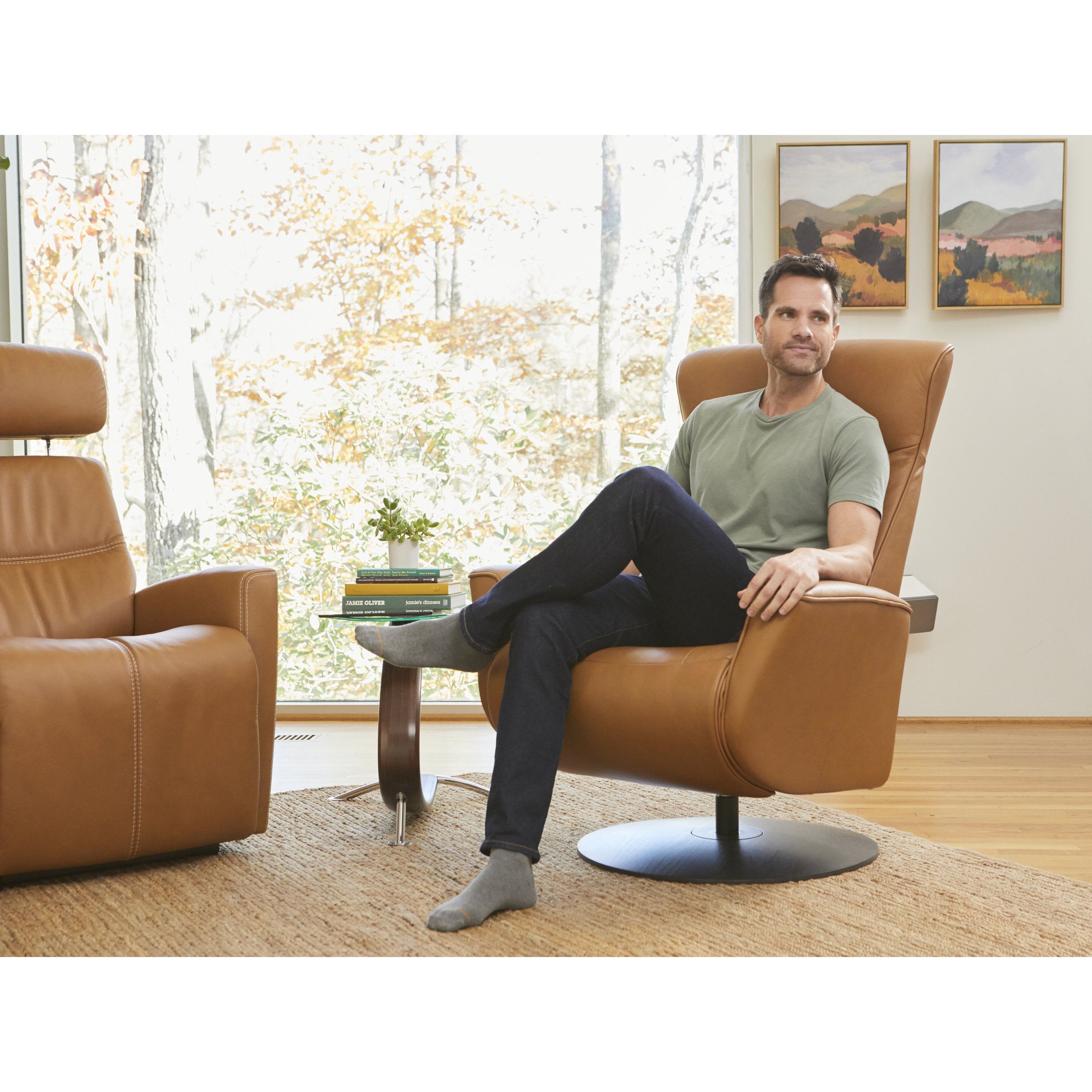 Man sitting in a brown leather armchair in a room with large windows and a view of trees.