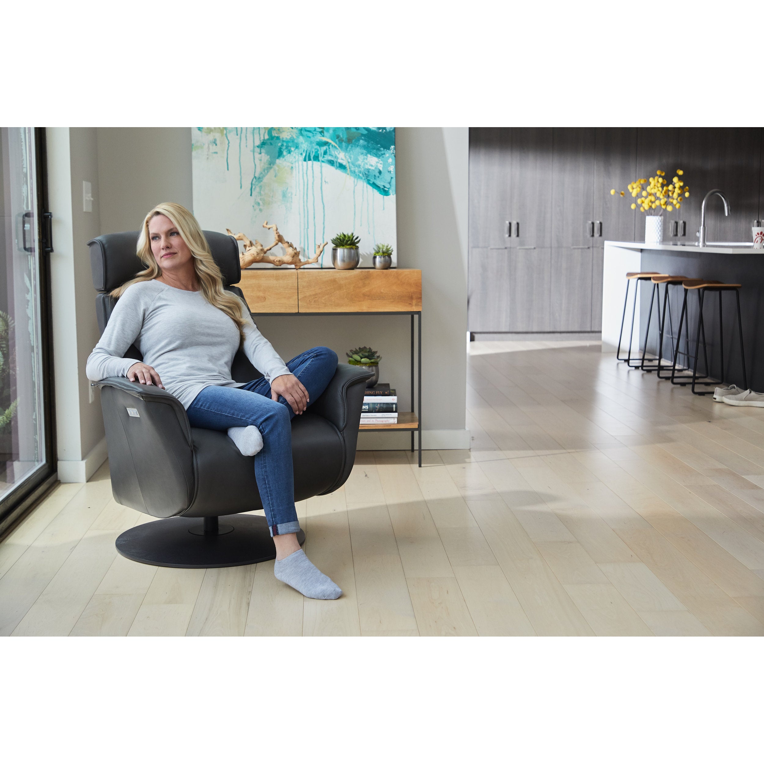 Woman sitting in a modern black chair in a home setting with a kitchen in the background.