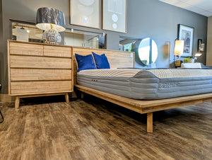 Bedroom with wooden bed frame, mattress, and dresser against a blue wall.