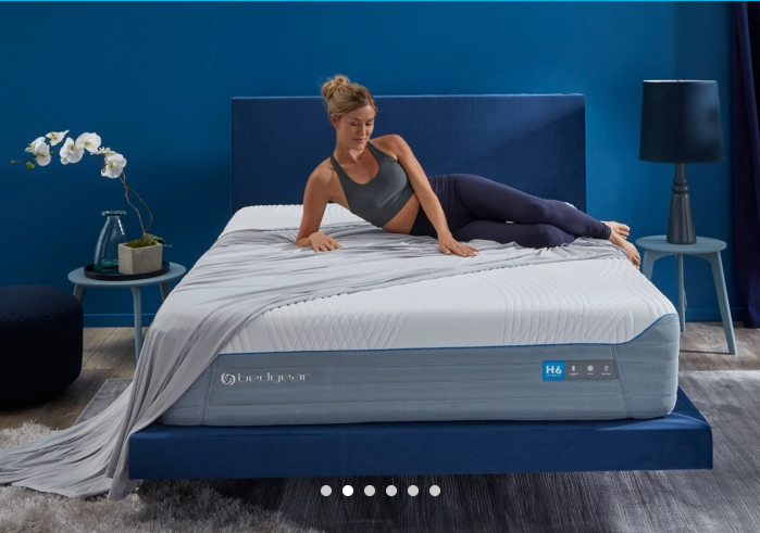 a memory foam mattress being shown on a blue bed frame base. person laying on it