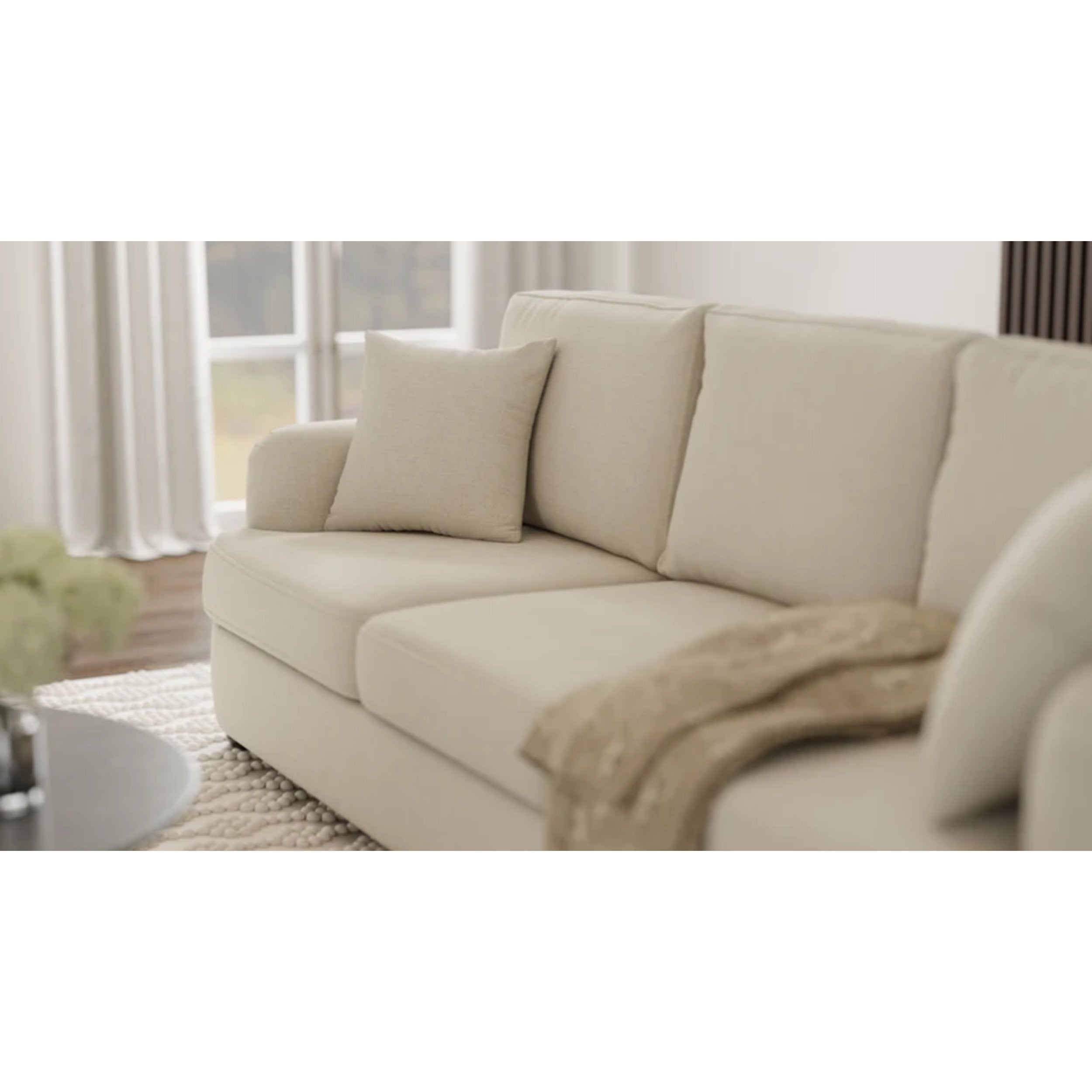 Beige sofa in a living room setting with curtains and a rug.