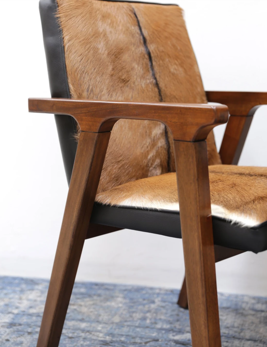 A leather armchair with a goat fur seat and solid oak wood frame, with a black leather backrest and seat cushion.